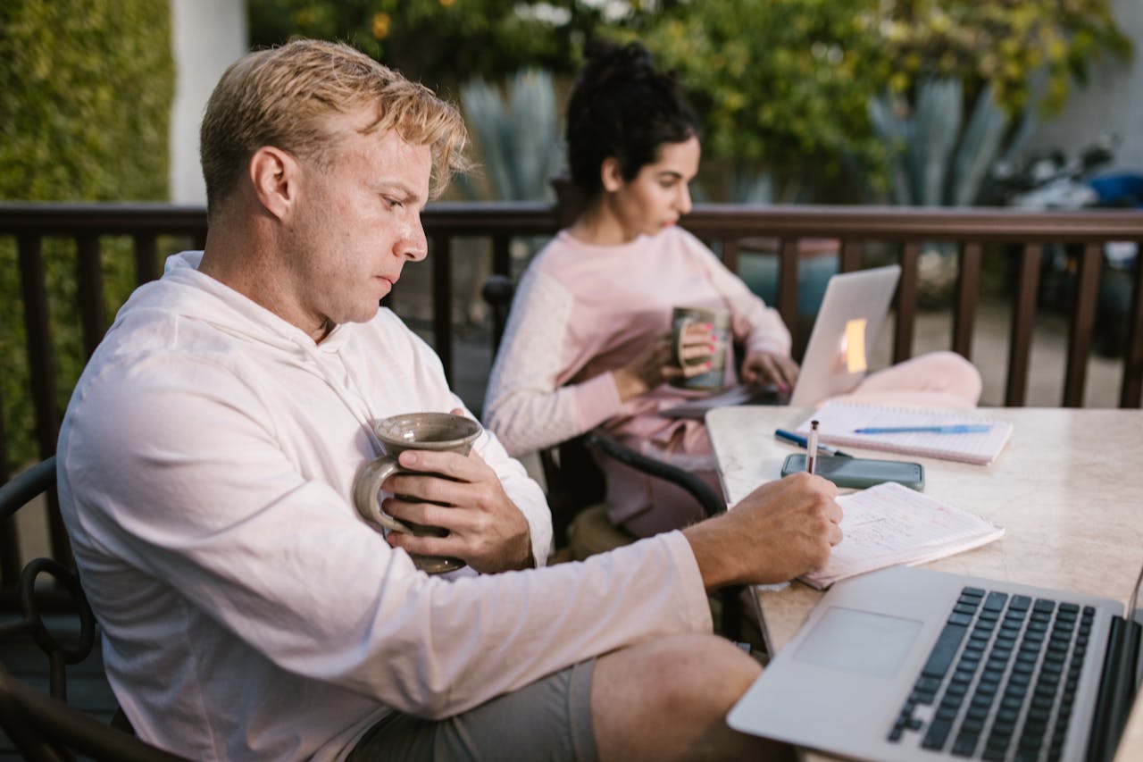 A couple working together on their laptops while enjoying a coffee outdoors.